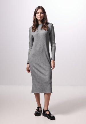 Langärmliges, eng anliegendes, geripptes graues Kleid mit Rundhalsausschnitt, knieumspielend, mit seitlichen Schlitzen, kombiniert mit schwarzen Plateauschuhen.