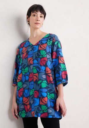Kleurrijke, loszittende tuniek van blauwe linnen met levendige bladvormen in rood, groen en zwart. V-hals en driekwart mouwen.