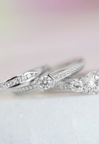 Trois bagues en argent ornées de diamants ronds et en forme de poire, avec des montures complexes et des détails de bande présentant de petites pierres incrustées.