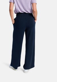 Marina vida byxor med vid ben och elastisk midja, sidfickor, gjorda av mjukt tyg. Bärs med vita sneakers och en ljuslila topp.