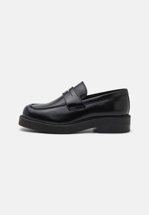 Mocassin en cuir noir avec un bout arrondi, des coutures décoratives à l'avant et une semelle en caoutchouc épaisse. Texture lisse avec une finition brillante.