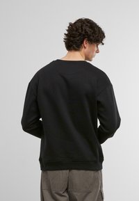 Svart genser med rund hals og senkede skuldre. Glatt tekstur, ribbede mansjetter og kant, kombinert med avslappede beige bukser.