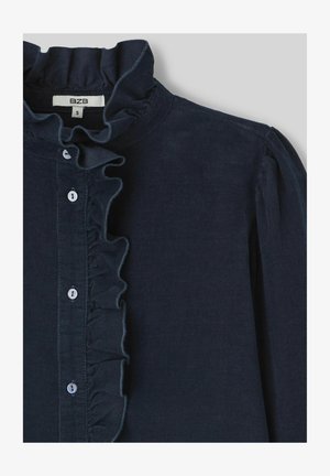 Chemise en velours côtelé bleu foncé avec un col froncé haut, une fermeture à boutons à l'avant et des manches légèrement bouffantes. Présente de petits boutons blancs.