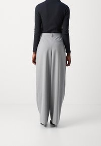Breda grå byxor i texturerat tyg, med en bakficka och hög midja, kombinerat med en svart långärmad topp.