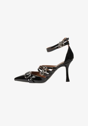 Zapato de charol negro de tacón alto con punta afilada, correa en el tobillo y múltiples hebillas decorativas en la parte frontal. Textura suave.