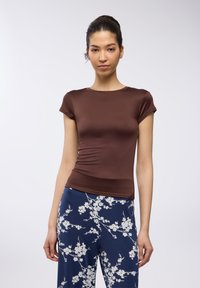 T-shirt aderente marrone con maniche corte, realizzata in tessuto liscio. Abbinato a pantaloni blu navy con motivi floreali bianchi.