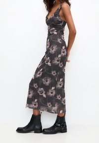 Robe midi florale avec un fond gris foncé, ornée de grandes fleurs rosâtres et d'un design ajusté. Portée avec des bottines noires.