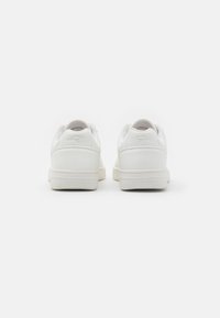 Weiße Sportschuhe mit einem glatten Lederoberteil und strukturierten Mesh-Akzenten. Minimalistisches Design mit runder Zehenpartie und flacher Sohle.