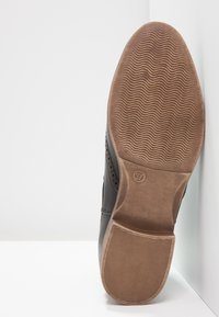 Scarpa in pelle nera con suola in gomma marrone texture. La parte inferiore presenta un motivo ondulato e un tacco accentuato da un design cucito. Taglia 37.