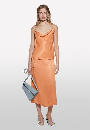 Top in satin arancione senza maniche con collo a cowl abbinato a una gonna midi. Accessoriato con una borsa azzurra chiara e sandali con tacco argento.