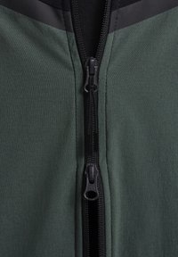 Chaqueta verde oscuro con una tela suave, un zipper negro con etiqueta YKK y acentos negros contrastantes en los hombros.