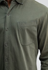 Olijfgroene blouse met knopen, gemaakt van zachte stof, met een borstzakje met gestikte details en een textuurrijke afwerking.