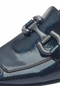 Glänzender marineblauer Schuh aus glänzendem Leder mit strukturierten Details. Verfügt über eine dekorative metallische Schnalle mit gerillten Akzenten.