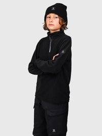 Bambino con capelli di lunghezza media che indossa un berretto nero, una felpa nera con zip e pantaloni cargo neri, con le braccia incrociate, su uno sfondo neutro.