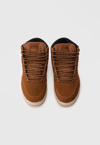 Smeđe antilop tenisice visokog gornjeg dijela s tamnim pertlama, kremastim gumenim potplatom i podstavljenim ovratnicima. Na jeziku tenisice nalazi se mali logo.