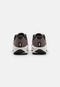 Buty sportowe z siateczkową cholewką w ciemnoszarym i beżowym kolorze, z miękką amortyzacją i teksturowaną czarną gumową podeszwą.