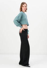 Kuttet, teal kabelstrikket genser med ballongsleeves, kombinert med høyt liv svarte vide bukser og spisse svarte hæler.