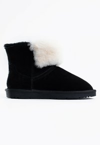 Botín de ante negro con un suave puño de piel blanca, suela plana negra y un diseño sencillo, con costuras visibles a lo largo de los bordes.