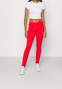 Röda sportbyxor med vita sidosträck, elastisk midja och sidofickor, kombinerade med en figurnära vit kortärmad t-shirt.
