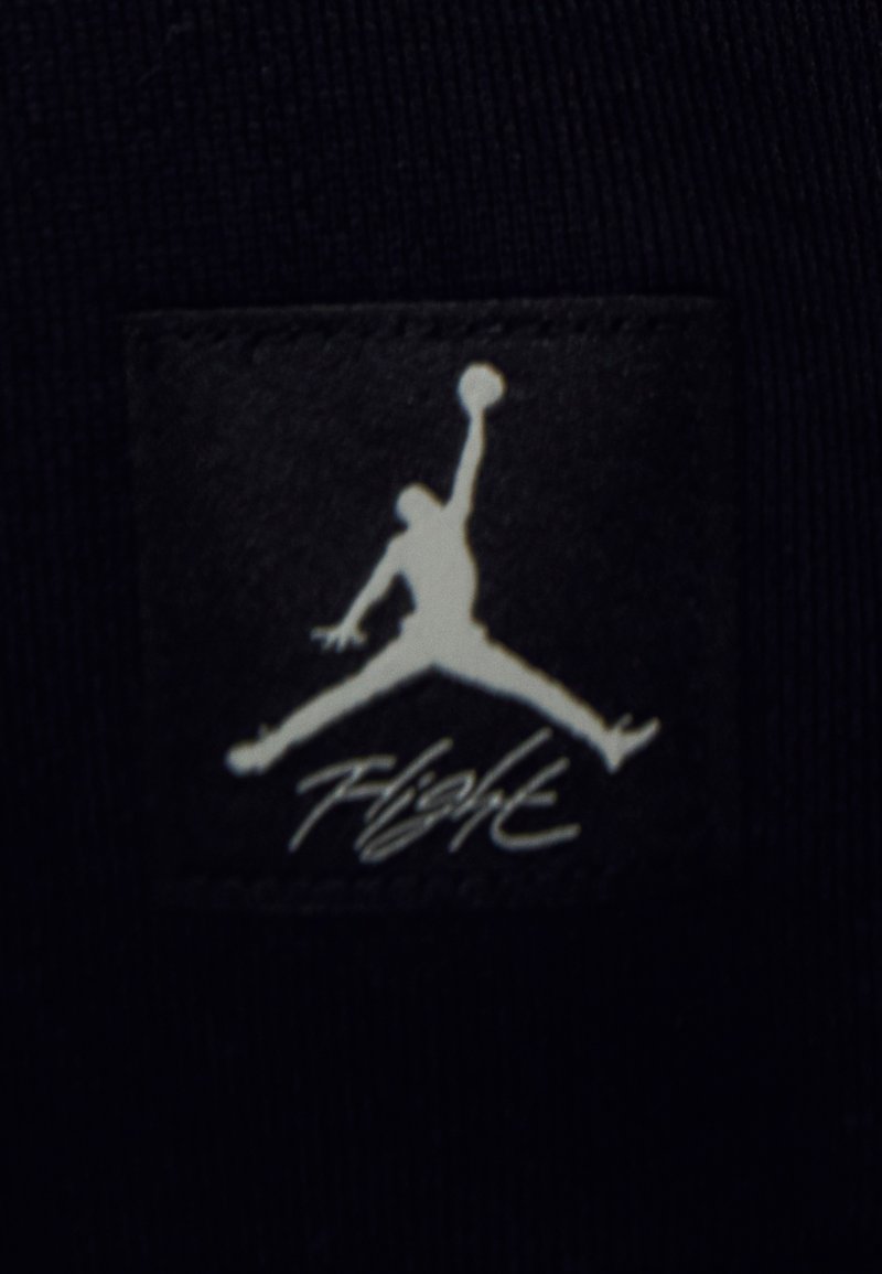 Parcha de tela negra con la silueta blanca de un jugador de baloncesto en una pose de salto, con el texto "Vuelo" debajo en una escritura fluida.