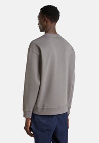 Sweatshirt gris avec une coupe décontractée, col et poignets côtelés, et en tissu doux en mélange de coton. Détails de couture visibles au dos.