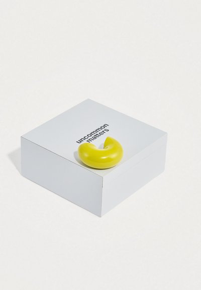 Κίτρινο γυαλιστερό κεραμικό αντικείμενο σε σχήμα ημισελήνου πάνω σε λευκό κουτί με το κείμενο «uncommon matters» τυπωμένο στην κορυφή.