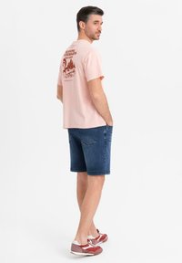 Camiseta de algodón rosa claro con un gráfico de "Entusiastas del running" en la parte de atrás, combinada con pantalones cortos de mezclilla azules y zapatillas deportivas rojas y blancas.