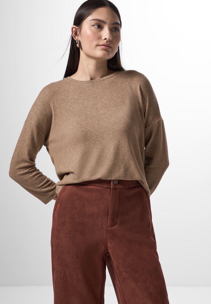 Brauner langärmeliger Pullover aus weichem Stoff mit lockerer Passform, kombiniert mit rostfarbenen Wildlederhosen mit vorderem Knopf und Taschen.