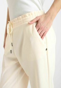 Licht beige broeken met een ontspannen pasvorm, trekkoord in de taille en zijzakken. Gemaakt van een gladde stof met een subtiele glans, voorzien van zwarte accenten.