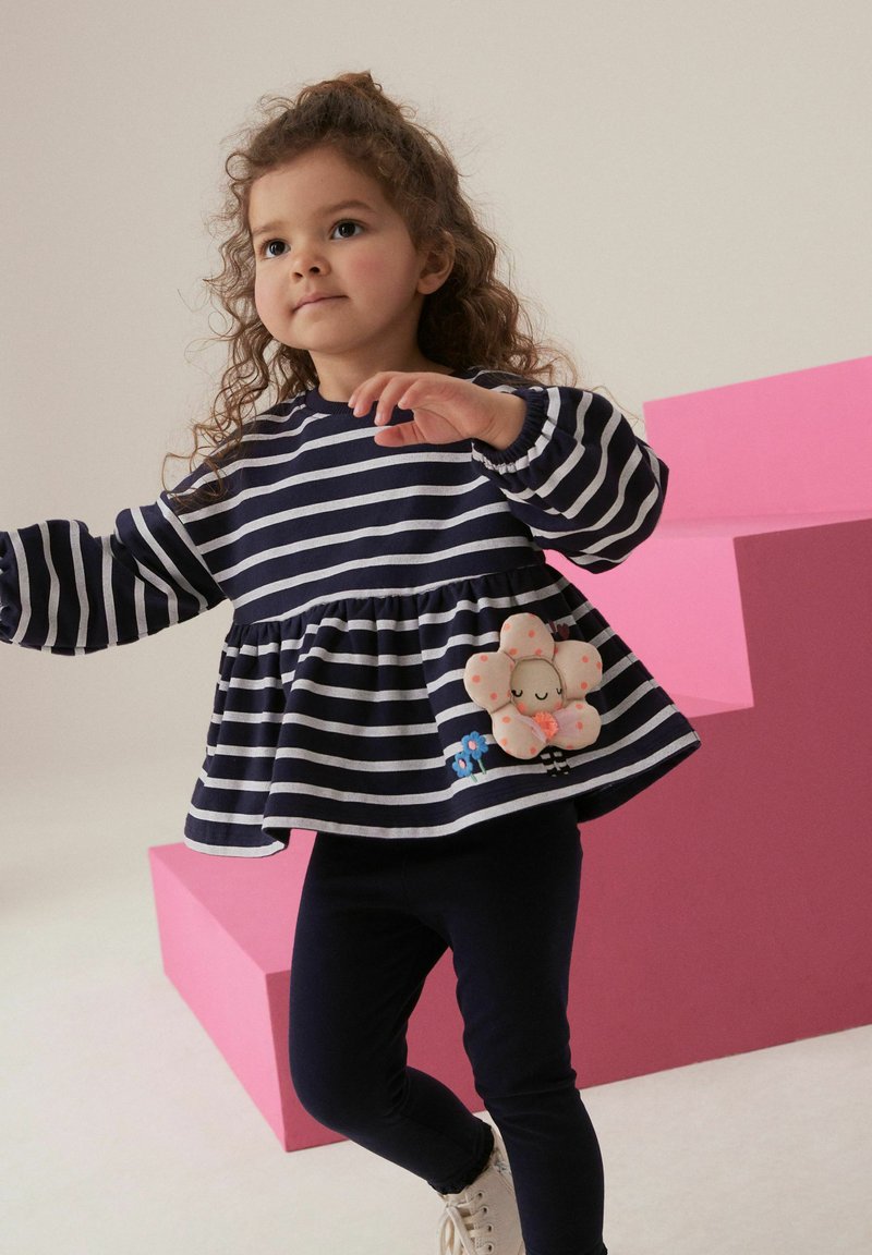 Tumesinise ja valge triibuline pikakä sleeve top, millel on peplum-äär ja lilleline fliisaplikatsioon ning sinine lilletikand. Kombineeritud tumedate legging'itega.
