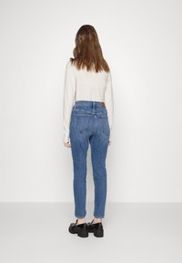Vaqueros de denim azul de talle alto con un diseño ajustado, estilo de cinco bolsillos y una etiqueta de cuero marrón en la parte superior de la cintura.
