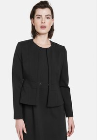 Schwarzer strukturierten Blazer mit langen Ärmeln, kleinem Rundhalsausschnitt, vorderem Verschluss und taillierter Passform mit dezenten Nahtdetails.