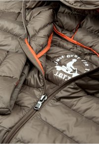 Bruine gewatteerde jas met een oranje binnenvoering, uitgerust met een zilveren rits en een logo op de stof. Gelaagde, gewatteerde uitvoering.