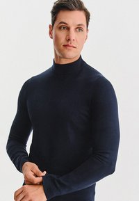 Granatowy sweter z golfem wykonany z miękkiego materiału, dopasowany fason, długie rękawy zakończone prążkowanymi mankietami. Gładka faktura bez wzorów.