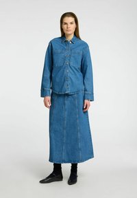 Denimová košile v středně modré barvě, na knoflíky, se dvěma náprsními kapsami. Ladící dlouhá denimová sukně má rovný, áčkový střih a kontrastní švy.