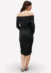 Robe noire épaule dénudée avec texture froncée, coupe ajustée, longueur genou, manches longues et tissu doux. Chaussures ton argenté.