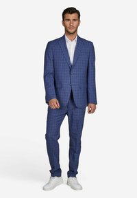 Blauwe geruite pak gemaakt van lichte stof, met een blazer met één knoop en taps toelopende broeken, gecombineerd met witte sneakers.
