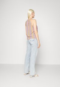 Top sem mangas multicolorido com um padrão; emparelhado com jeans de perna larga azul-claro e sandálias de salto bejes. Fundo digital.