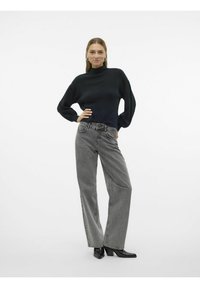 Svart ribbad turtlenecktröja med långa ärmar i kombination med högmidjade grå vida jeans. Svarta klackstövlar fulländar outfiten.