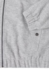 Chaqueta de lana gris con cierre frontal con cremallera, puños acanalados y detalle de botón a presión. Textura suave con una cintura ajustada y elástica.