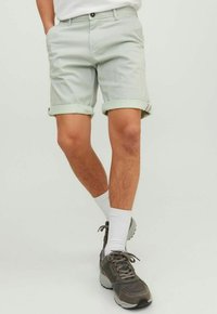 Lichtgroene gestreepte shorts met opgerolde manchetten, gedragen met witte sokken en grijze sportschoenen, wat een casual zomerse look laat zien.