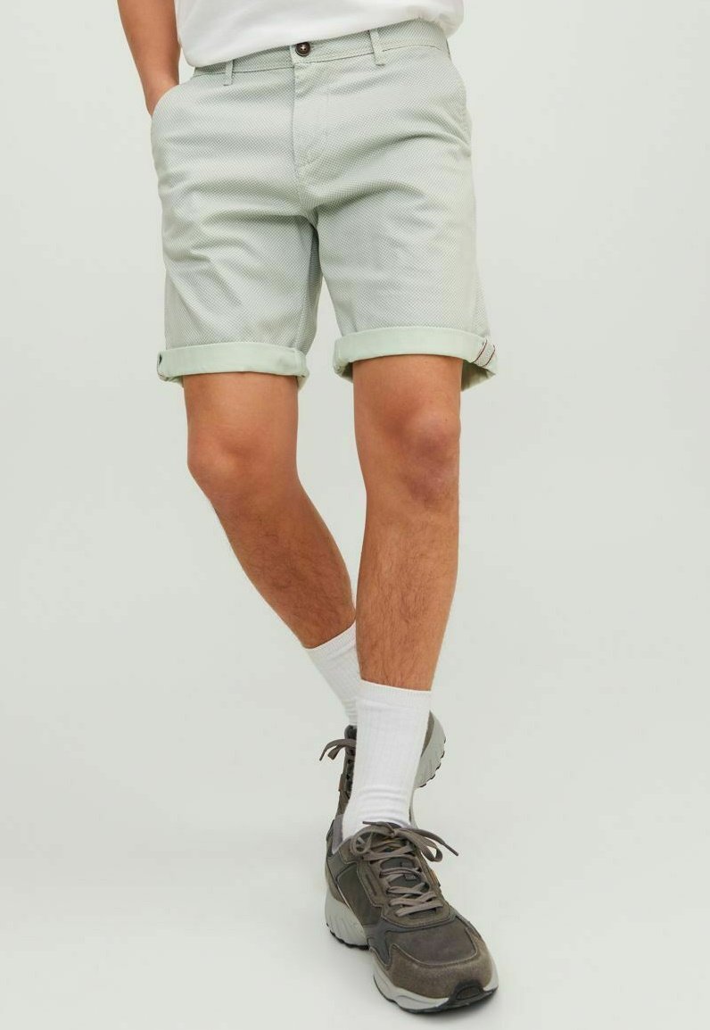 Lichtgroene gestreepte shorts met opgerolde manchetten, gedragen met witte sokken en grijze sportschoenen, wat een casual zomerse look laat zien.