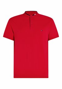 Röd polo skjorta med ståkrage, knäppning med tre knappar och liten logotyp på vänster bröst. Tillverkad av ett glatt, andningsbart material.