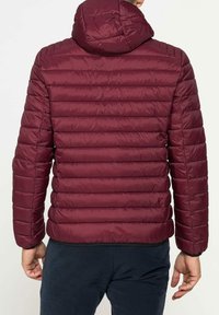 Giacca a vento bordeaux con cappuccio, cuciture orizzontali, materiale leggero e polsini elasticizzati, vista da dietro.