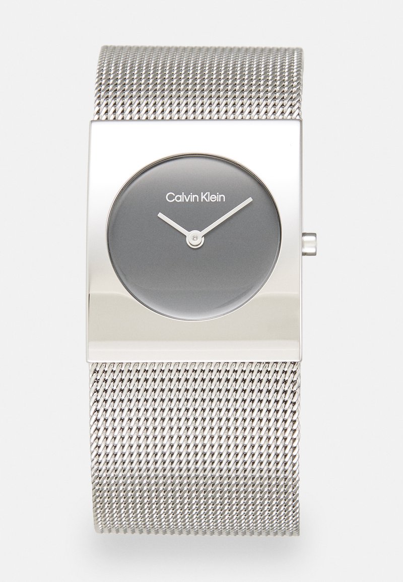 Montre avec bracelet en maille argentée, présentant un boîtier rectangulaire, un cadran gris et des aiguilles des heures et des minutes minimalistes blanches. Logo de la marque affiché à 12 heures.