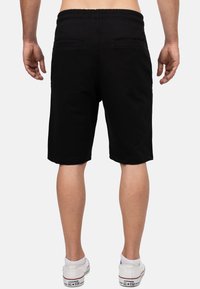 Zwarte katoenen shorts met een elastische tailleband, twee achterzakken en een relaxte pasvorm, gedragen met witte sneakers.