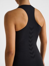 Woman wearing a black sleeveless athletic top with a racerback design and subtle chevron pattern down the spine.