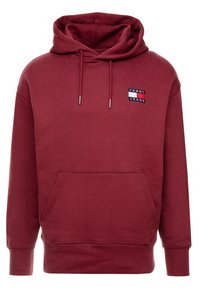 Bordowy hoodie z przednią kieszenią, kapturem ze sznurkiem, ściągaczami na rękawach oraz naszywką z logo na klatce piersiowej. Wykonany z miękkiej, teksturowanej tkaniny.