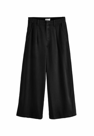 Schwarze, weit geschnittene Hosen aus weichem Denim, mit hoher Taille, Vorderfalten und Seitentaschen. Mit einem sauberen Saum und einem Etikett im Inneren abgeschlossen.
