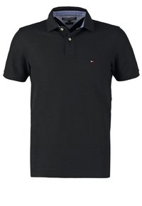 Musta poolpaita, joka on valmistettu puuvillasta, ja siinä on klassinen kaulus, kaksi nappia ja pieni brodeerattu logo vasemmassa rinnassa.